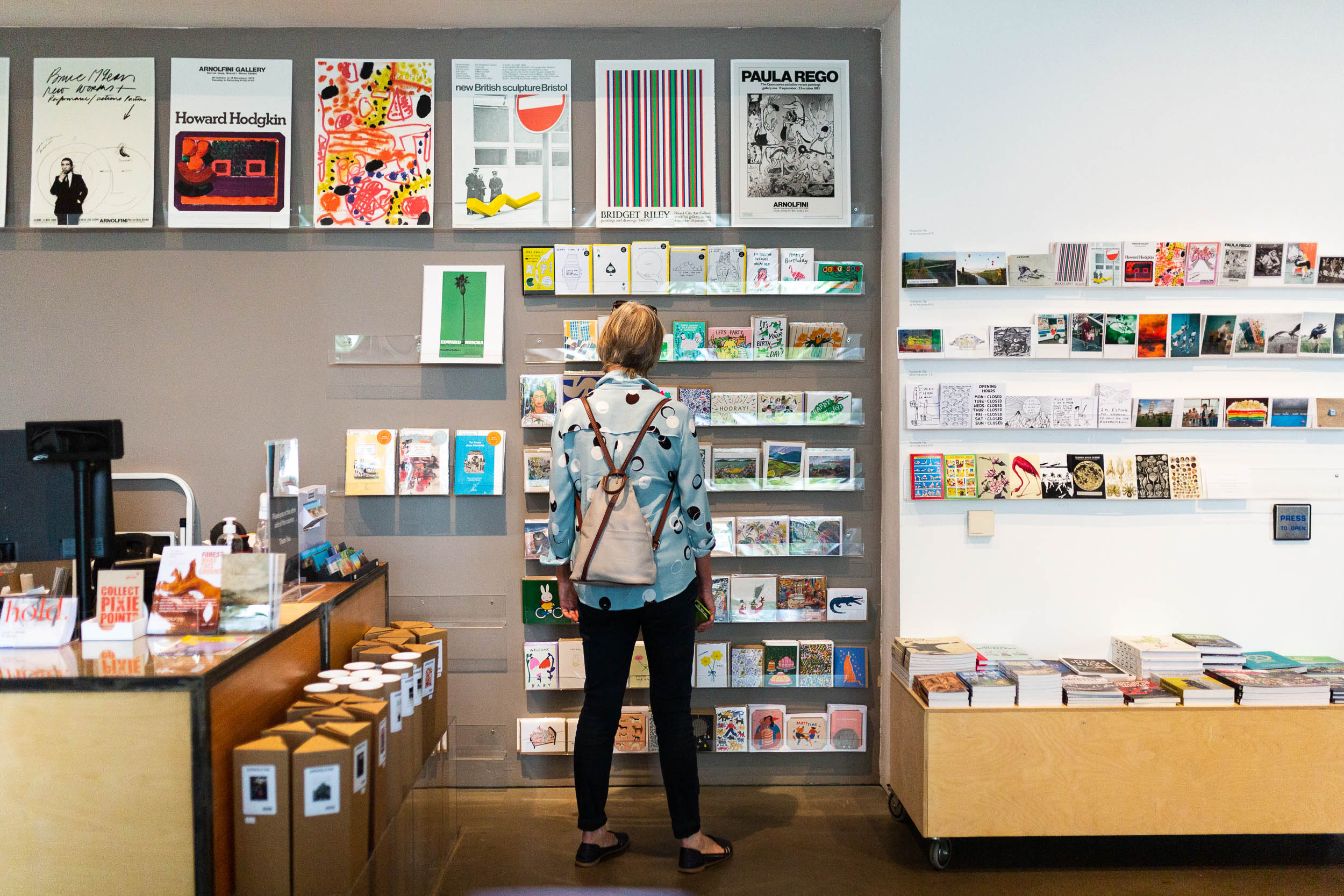 A colour photograph of a visitor in the Arnolfini Bookshop, looking through a selection of books on the shelf.