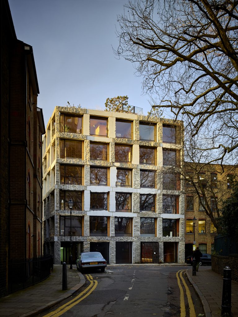15 Clerkenwell Close, a modern building in london, which celebrates quarried stone as a raw undressed material. The building is principally a 3d uniform grid of stone, with glass fronted cells. It is a sunny, clear, evening, and the top few floors of the building are gently lit with sunset sun.
