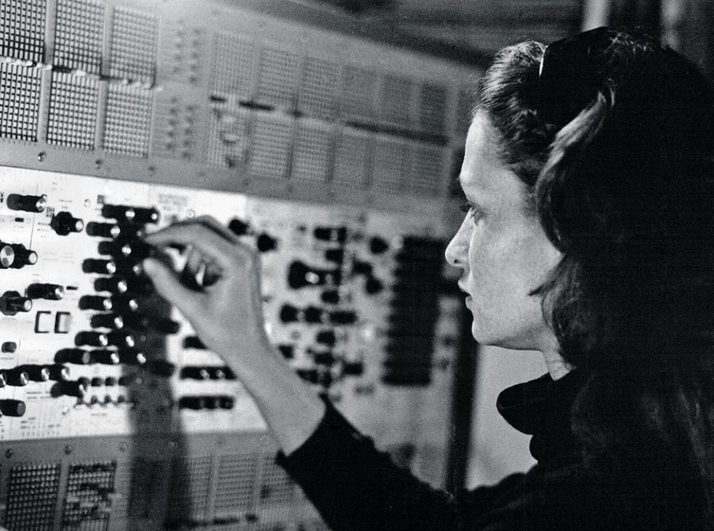 A black and white photograph of Elaine Radigue, working on a sound equipment, taken around 1970s by Yves Arman.