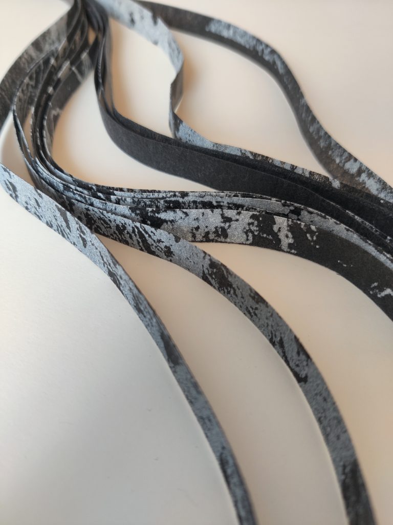 A colour photograph of strands of dark grey screen-printed fabric against a white background.