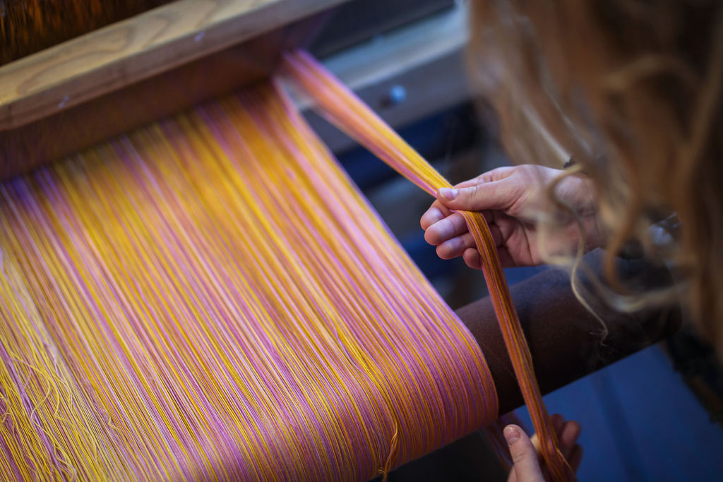 A pair of hands grab yellow and pink thread on a loom.