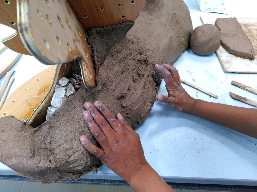 Hands scraping and building a clay sculpture