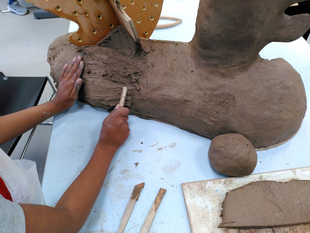 Close-up photograph of hands scraping and building a clay sculpture