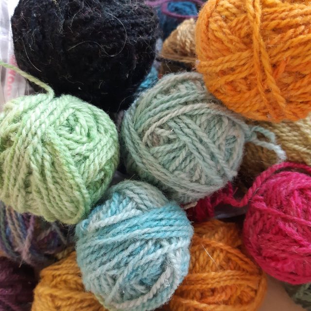 A coloured photograph of balls of yarns in green, blue, grey, black, orange and red.