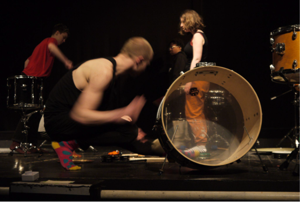 a blurred colour photograph of performers on stage taking part in the Ecstatic Drum Beats workshop.