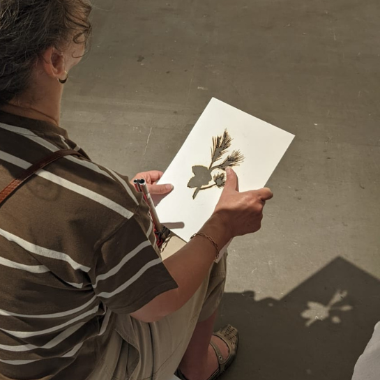 A coloured photograph of a person, holding an artwork example, by artist Rodrigo Arteaga,'s Monocultures for the Arnolfini's Visually Impaired Welcome Tour. A card, with a manually burnt leaf.