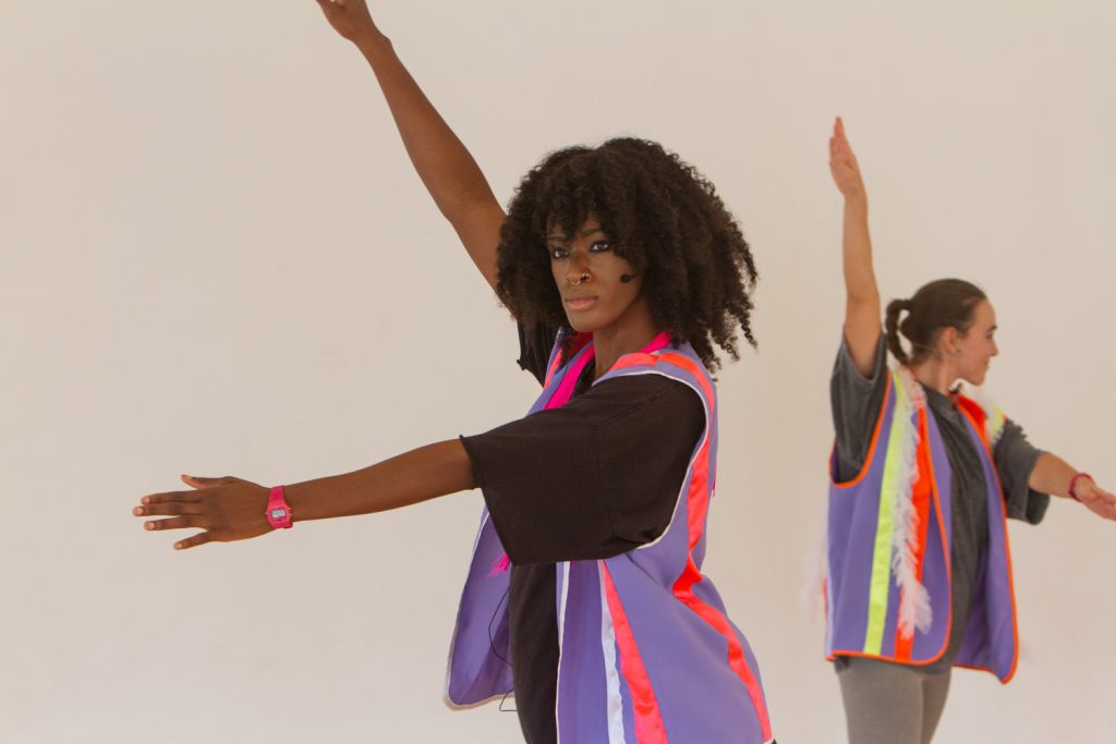 A coloured photograph of two Satelliser co-workers wearing hi-vis jackets, with arms wide apart, mid performance.