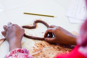 two hands are shaping a rolled out piece of clay into a heart shape