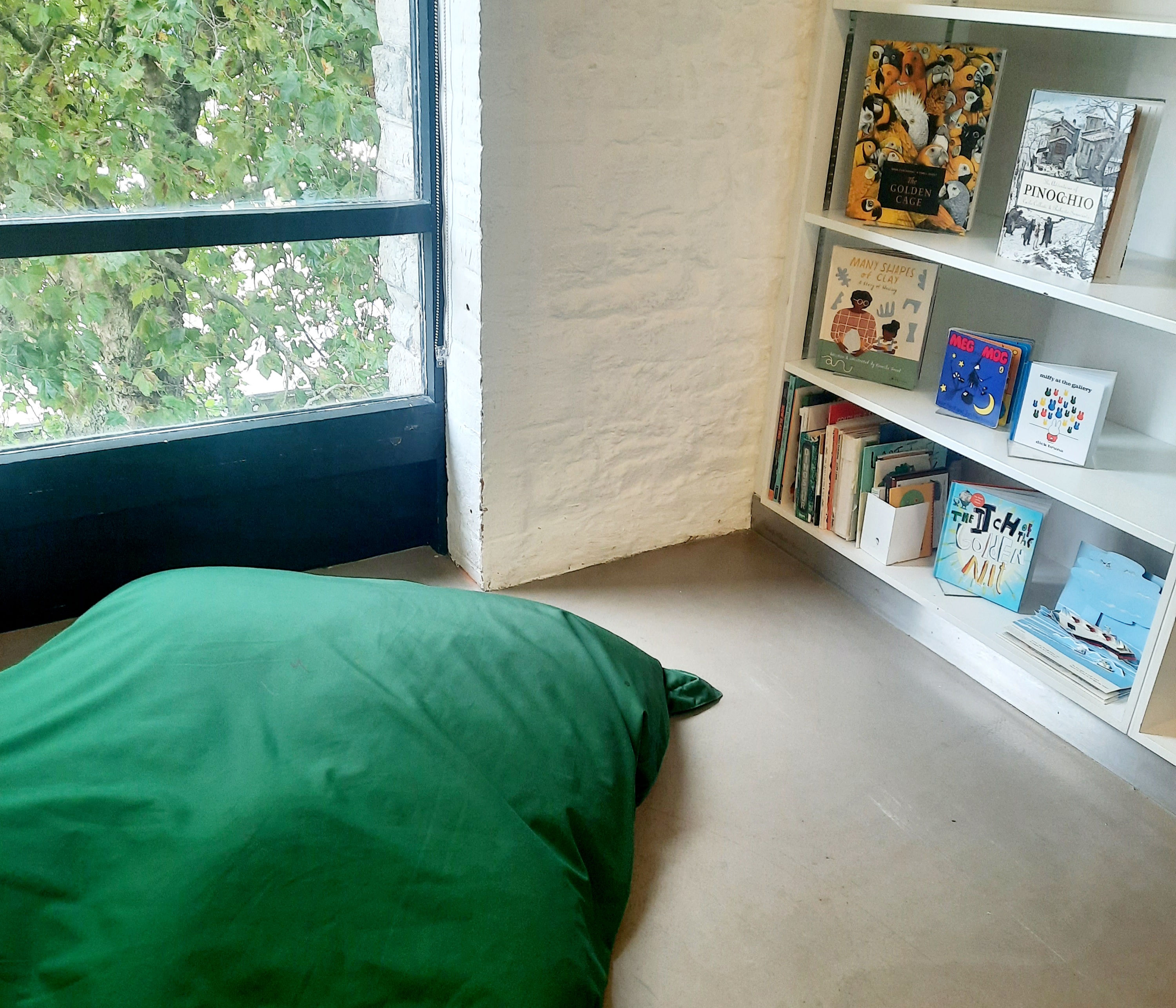 a colour photograph of some children's books on shelves, next to a window and a green bean bag in the Reading Room at Arnolfini.