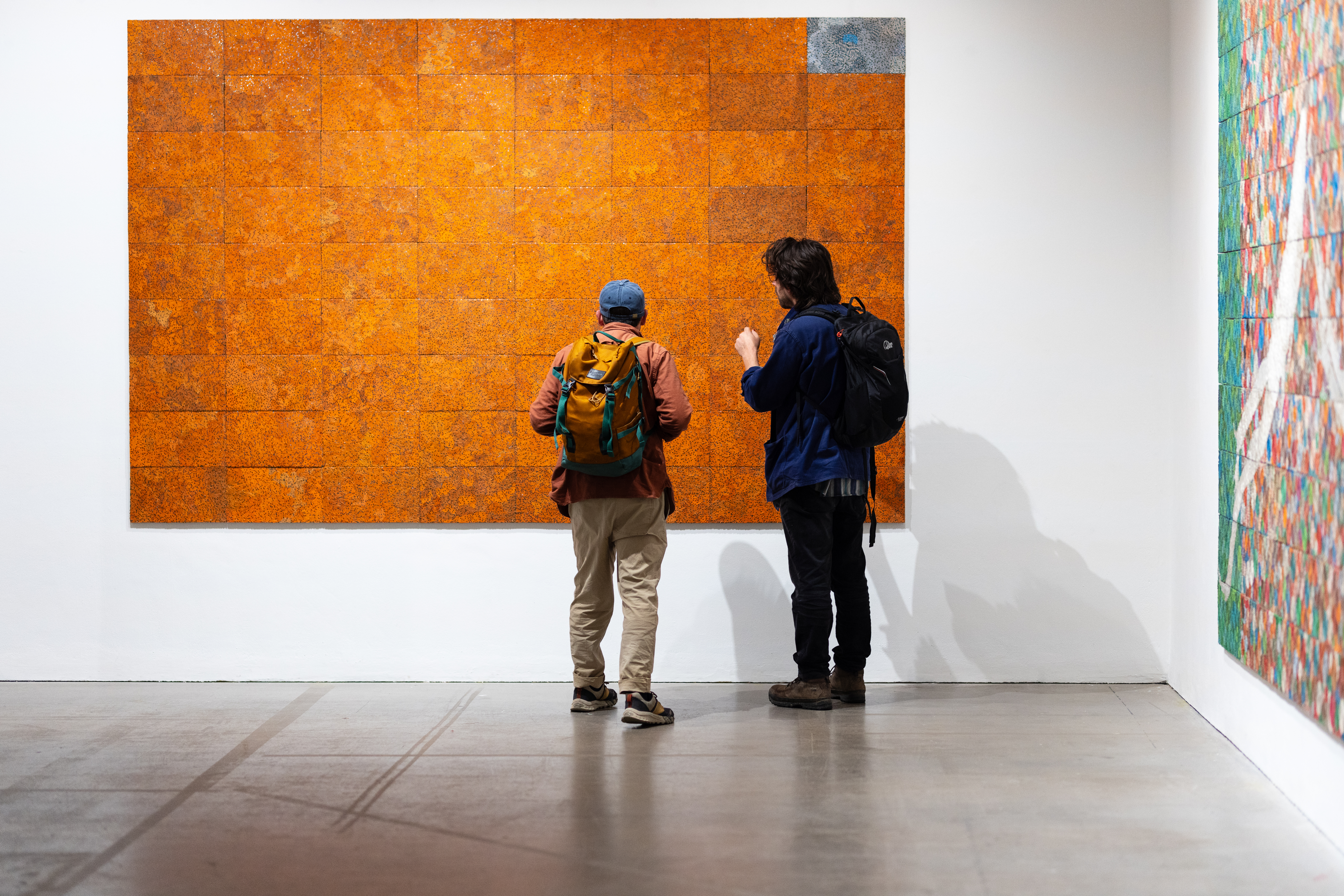 Two people standing in front of a large orange wall piece from the Eregata exhibition