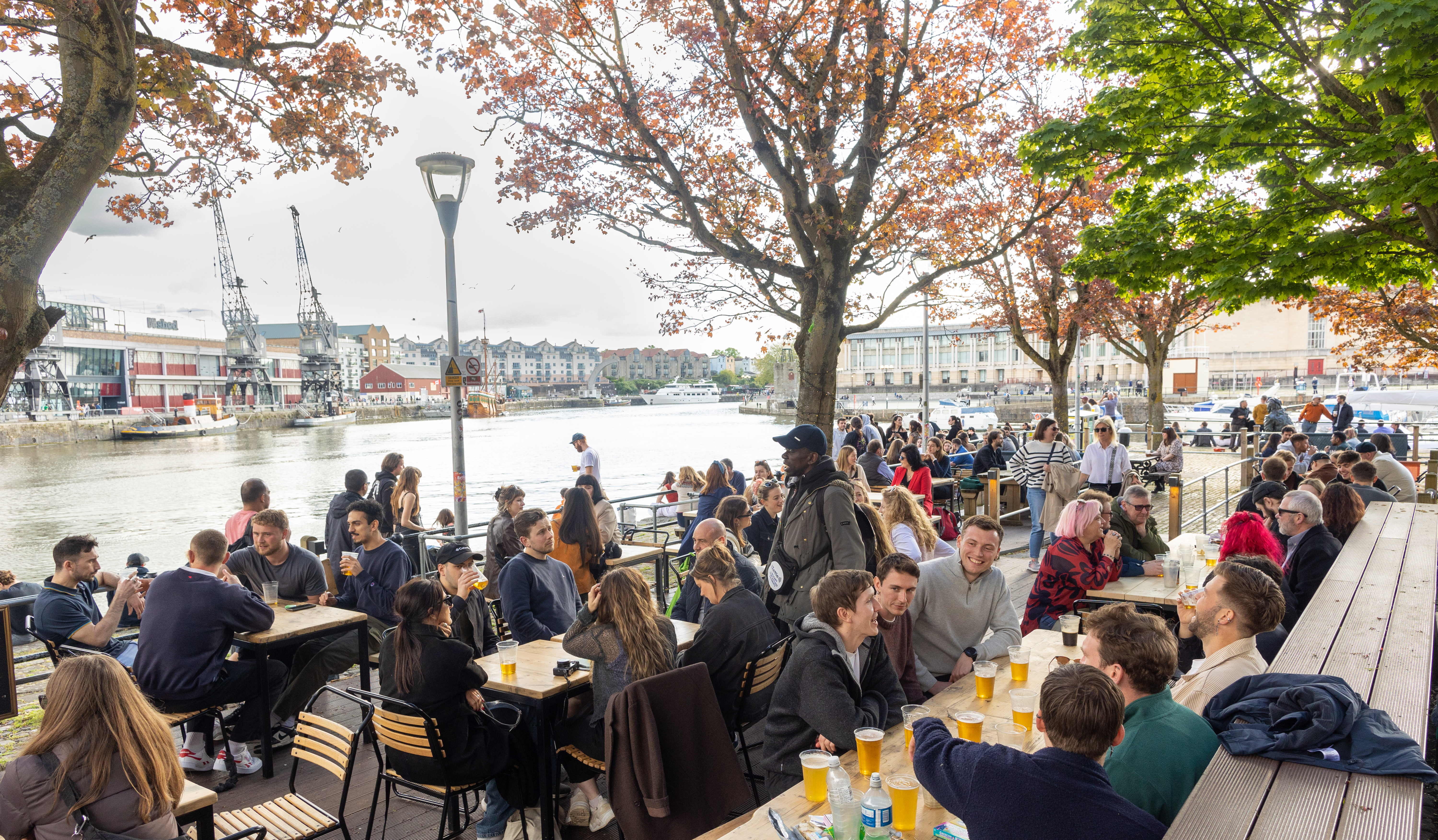 a colour photograph of a large number of people sat outside at the Arnolfini Cafe Bar on the Bristol harbourside